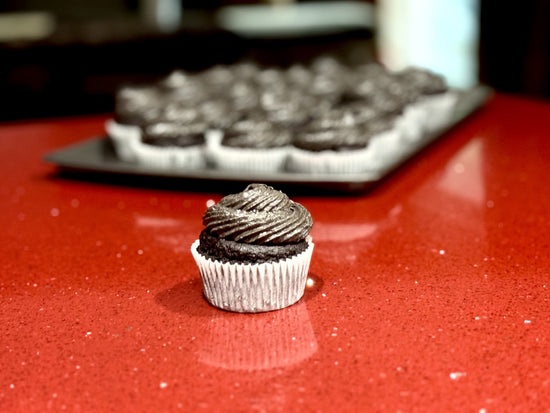 Image of dark chocolate cupcakes on a baking pan.  One cupcake is in the front of the picture.