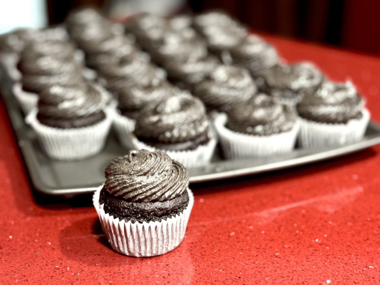 Image of dark chocolate cupcakes on a baking pan.  One cupcake is in the front of the picture.