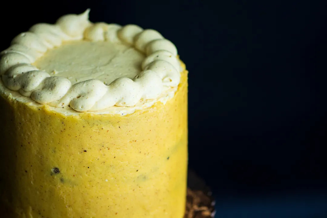 A close-up of a gluten-free caramel cake with white whipped frosting piped around the top edge, set against a dark navy background.