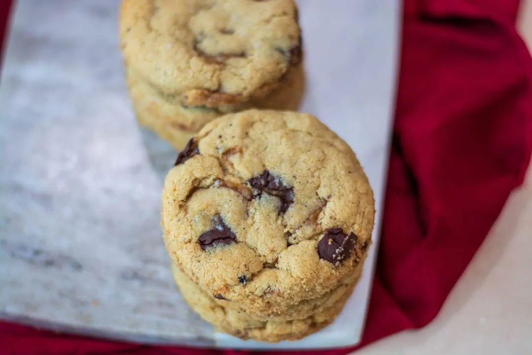 Golden-brown gluten-free chocolate chip cookies stacked on a white rectangular plate, with a red fabric napkin in the background.