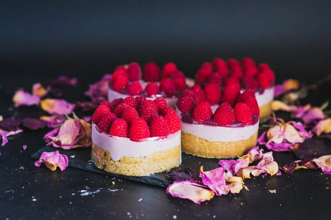 A minimalist luxury dessert spread displaying four individual Chipper & Cheeky gluten-free raspberry mousse mini cakes topped with fresh local raspberries, optimized for high-end dessert tables and corporate gifting.