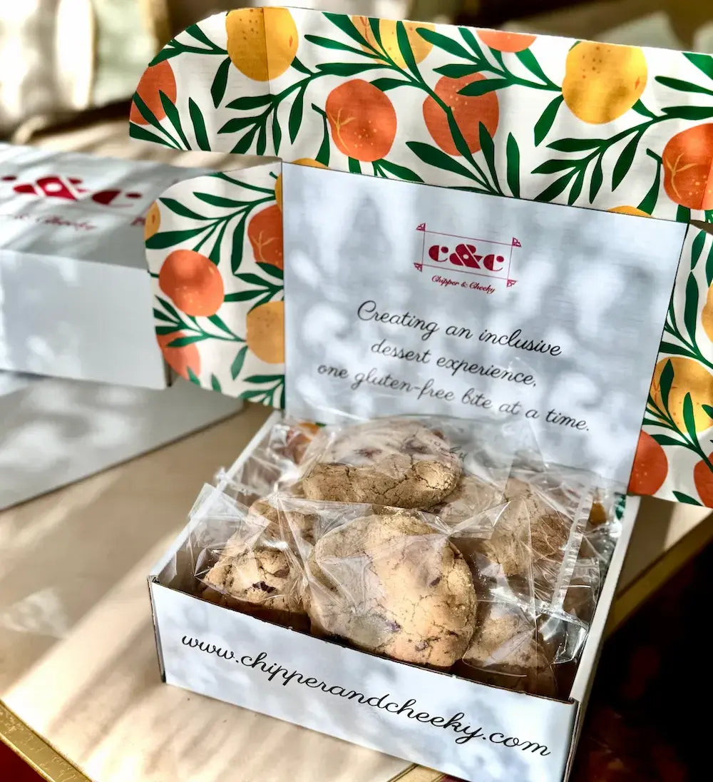 Box of shippable gluten-free cookies with a decorative lid featuring orange and leaf patterns, and a visible brand name, Chipper & Cheeky. 